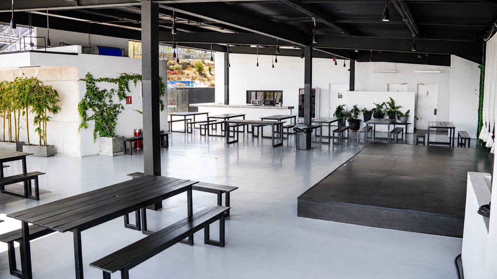 Zona de eventos techada, con mesas comunales, tarima y plantas